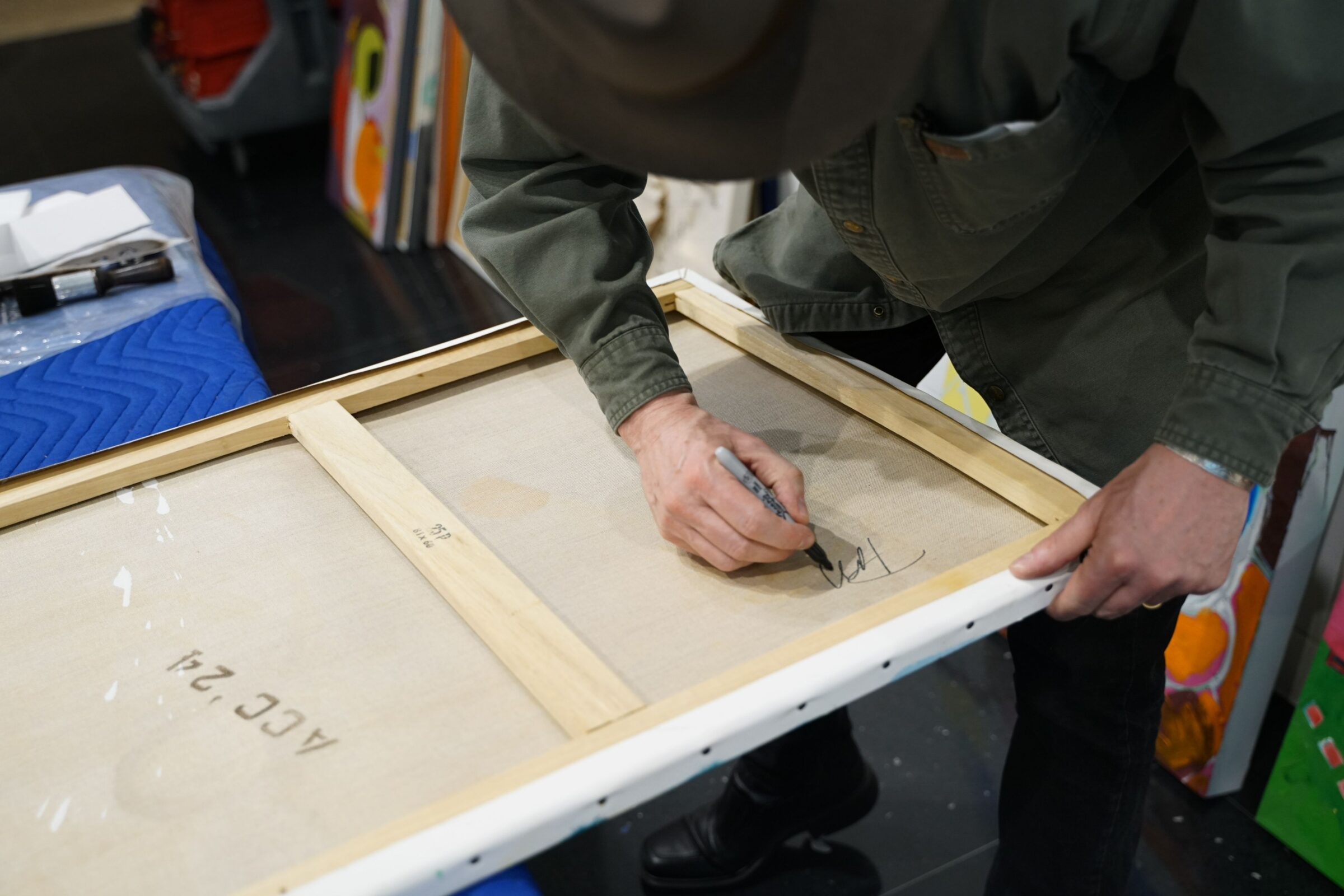 An artist signs the back of his canvas painting with a Sharpie marker.